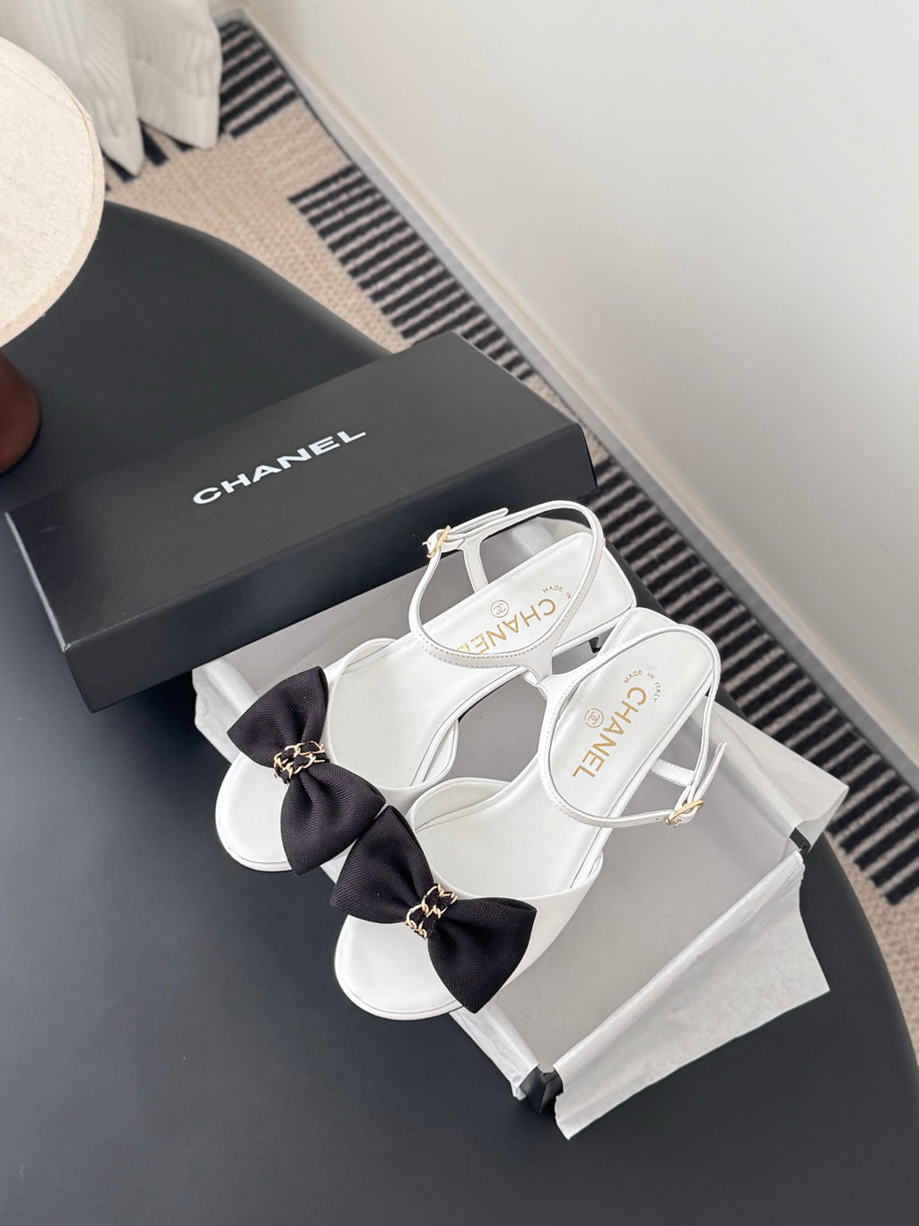 White open-toe slingback sandals with dark bow and gold-tone ankle strap hardware