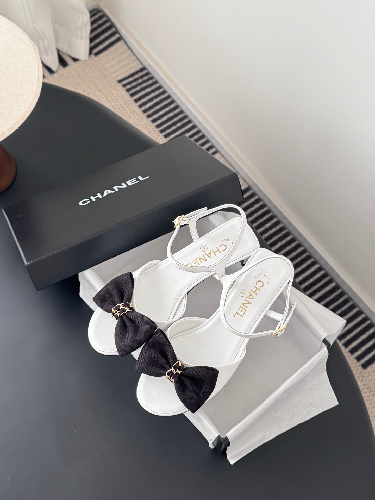 White open-toe slingback sandals with dark bow and gold-tone ankle strap hardware