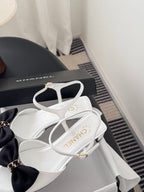 White sandals with dark bow, gold-tone chain ankle strap, open-toe slingback