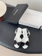 White open-toe sandals with dark bow and gold-tone ankle buckle, slingback strap