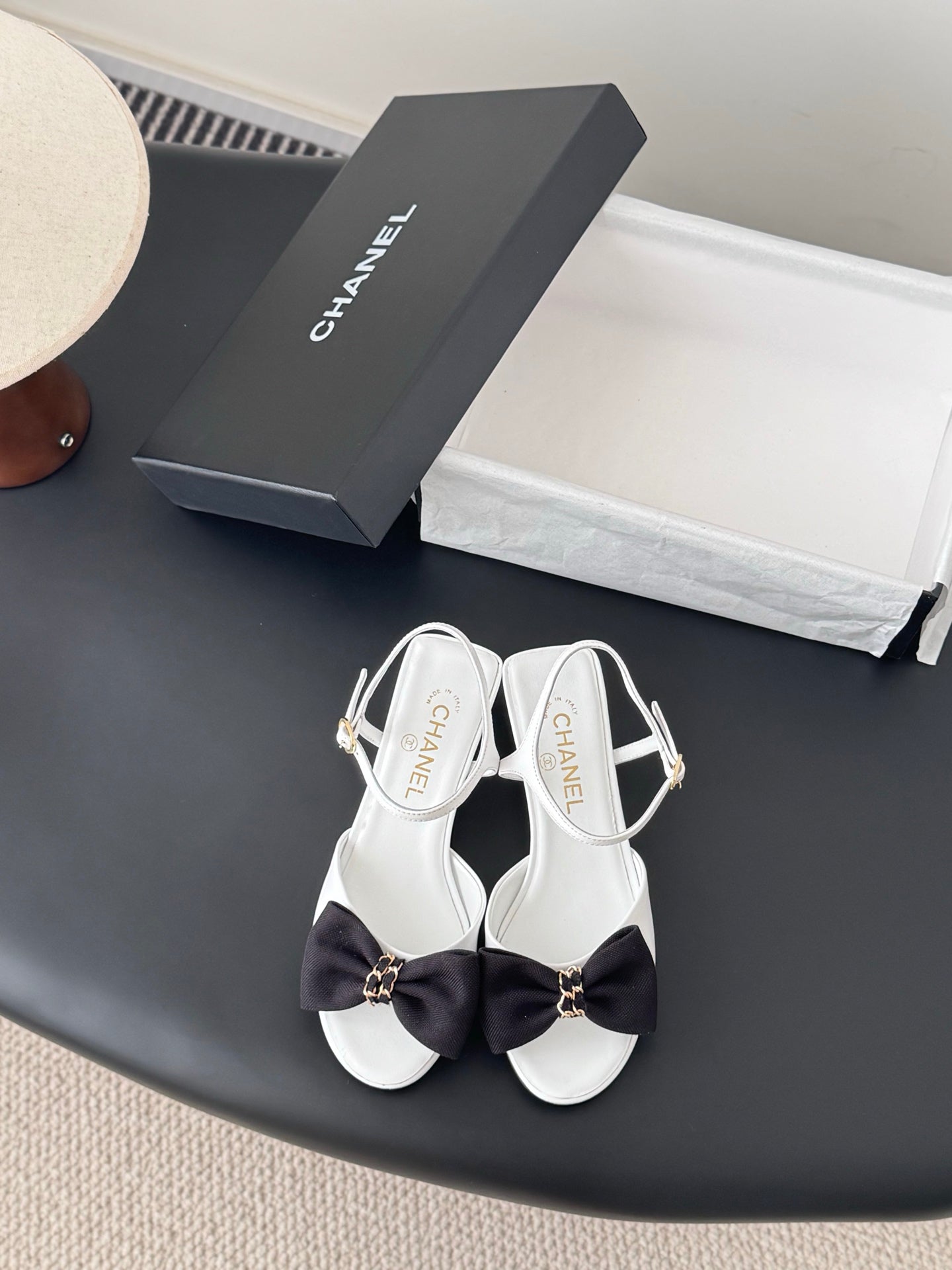 White open-toe sandals with dark bow and gold-tone ankle buckle, slingback strap