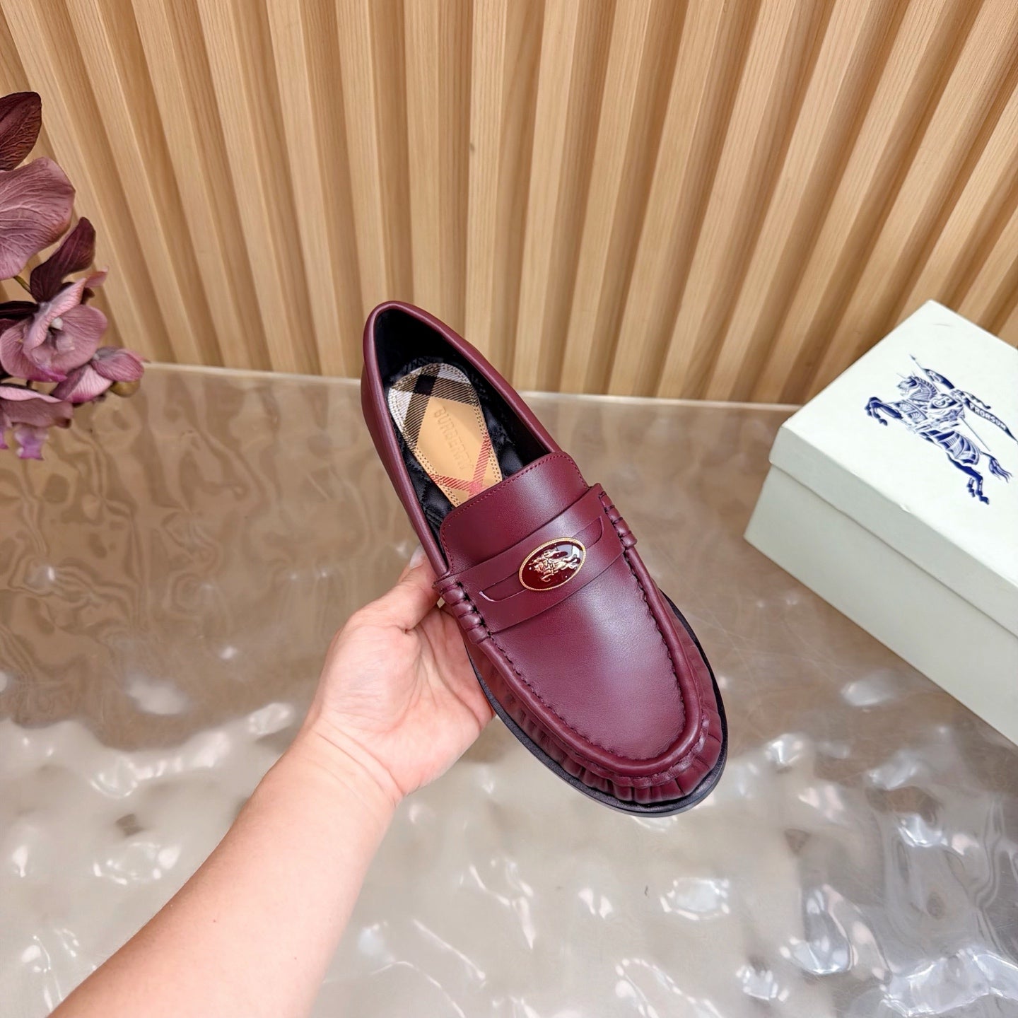 Burgundy leather loafer with gold crest and plaid lining, side view held