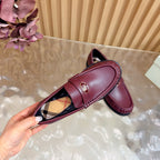Burgundy leather loafer with gold crest and plaid lining, close-up held view