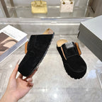 Black slip-on mule held in hand with tan lining, fur trim, and logo patch