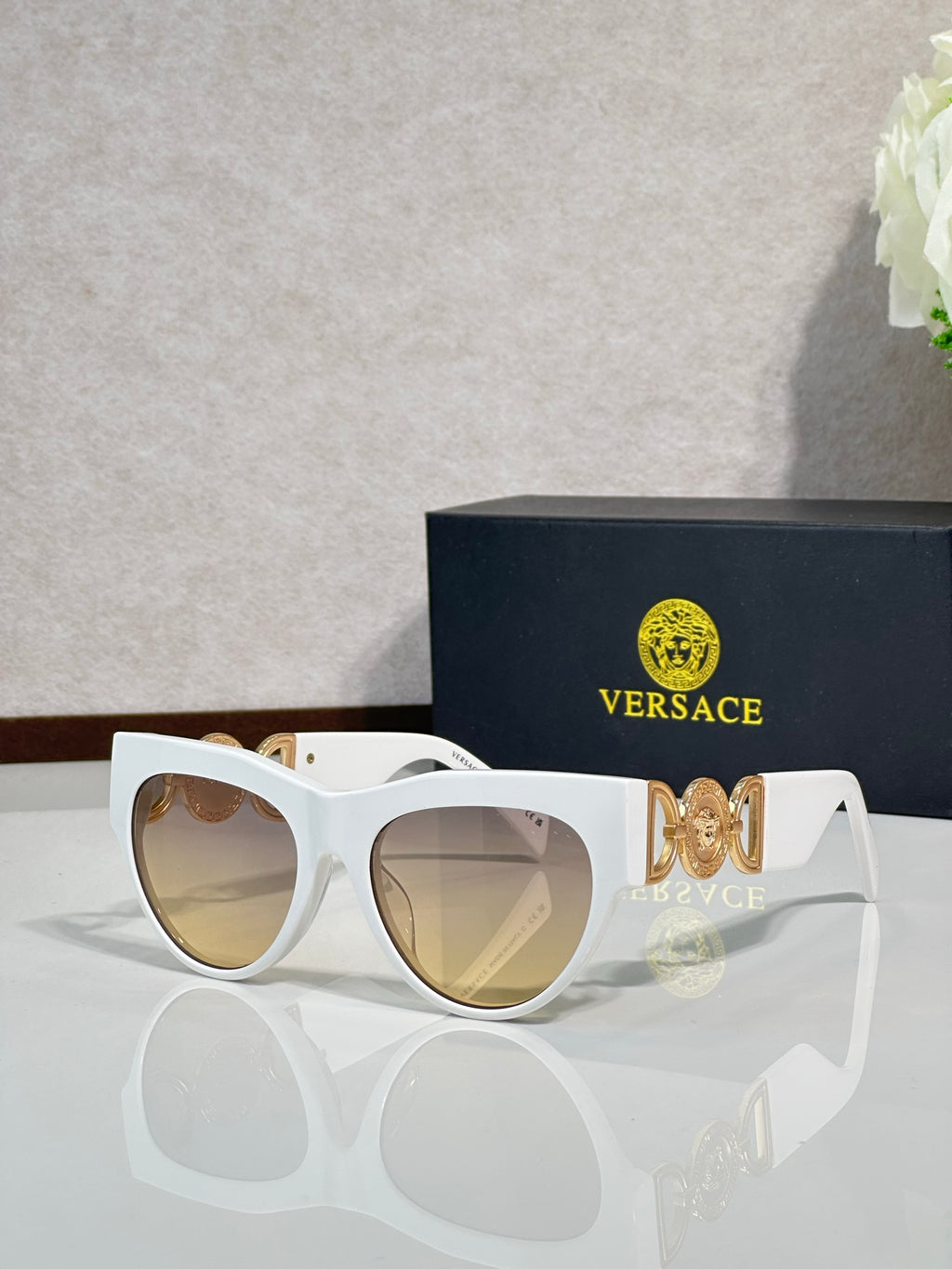 Sunglasses, white frames with gold emblem, tinted light lenses, rounded cat-eye