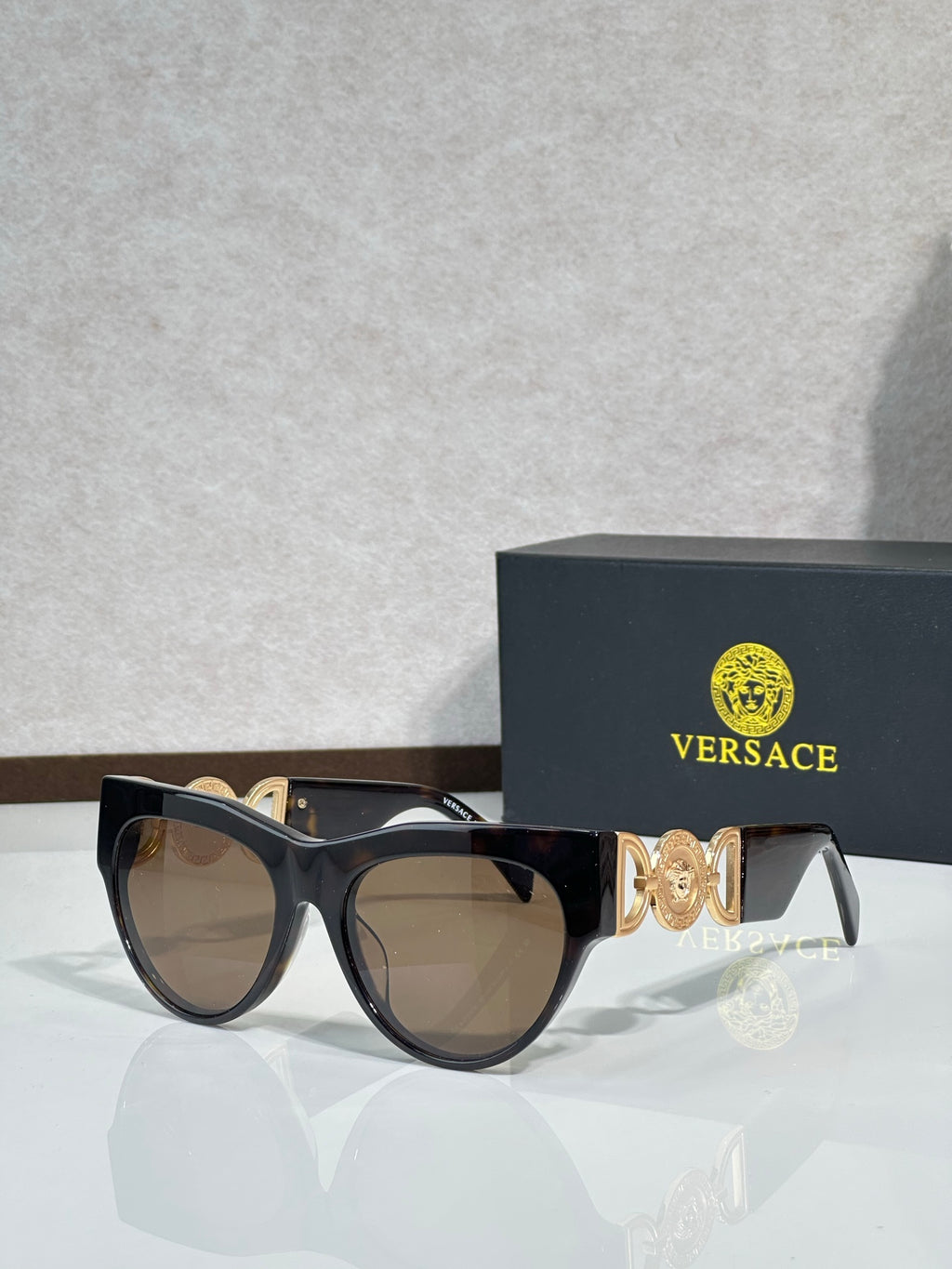 Sunglasses, black frames with gold emblem, tinted brown lenses, cat-eye style