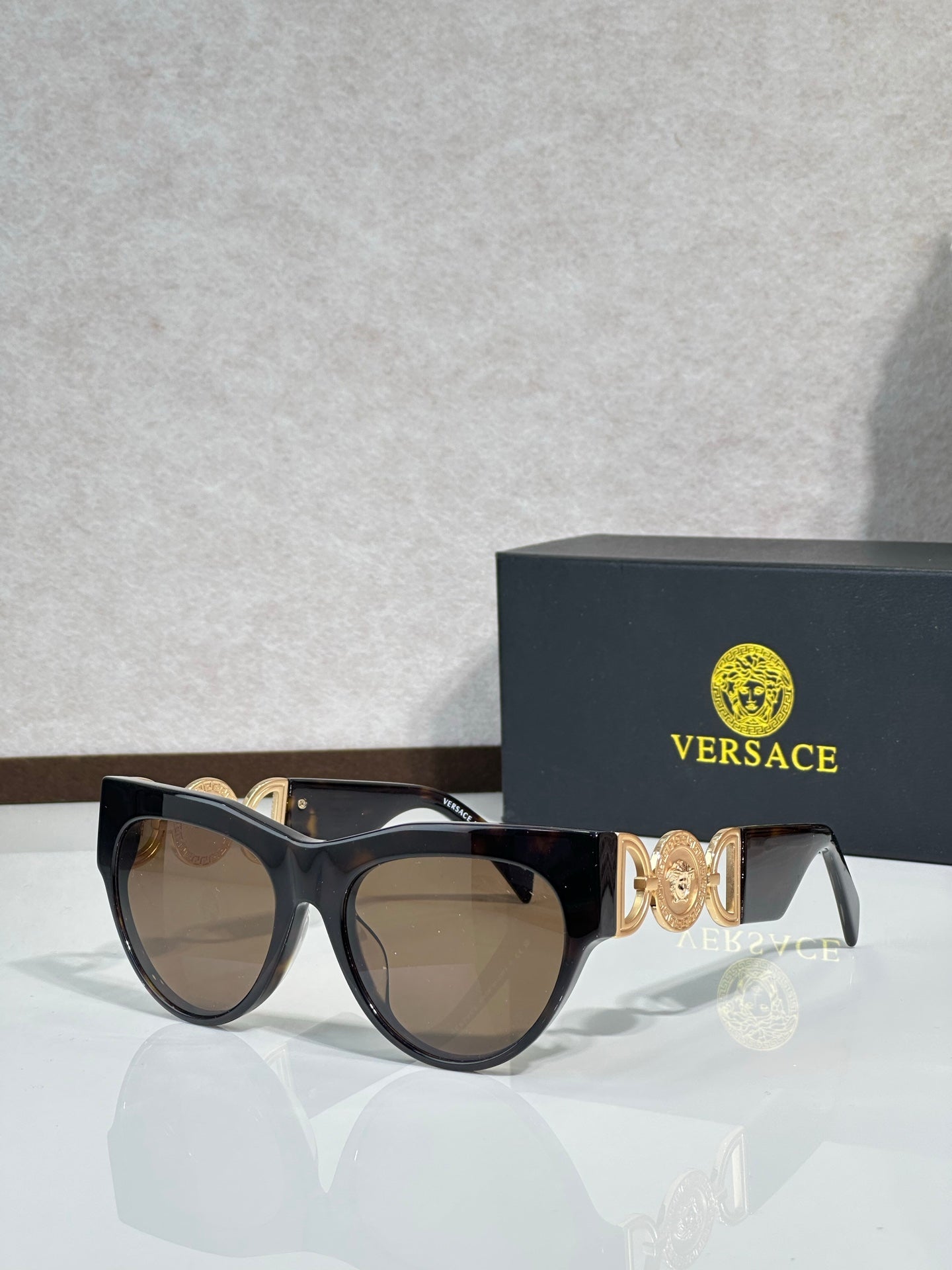 Sunglasses, black frames with gold emblem, tinted brown lenses, cat-eye style