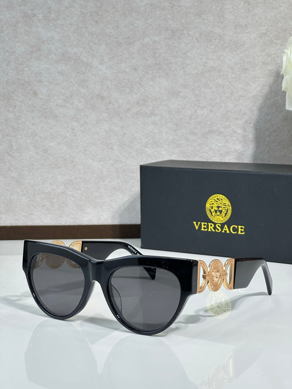 Sunglasses, black frames with gold emblem, tinted dark lenses, rounded cat-eye