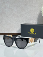Sunglasses, black frames with gold emblem, tinted dark lenses, rounded cat-eye