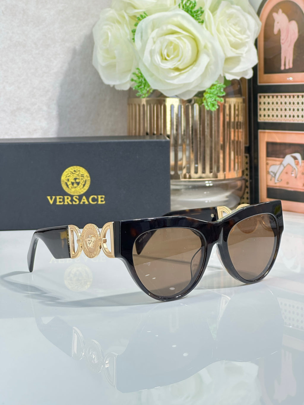 Sunglasses, black frames with gold emblem, gradient brown lenses, cat-eye style