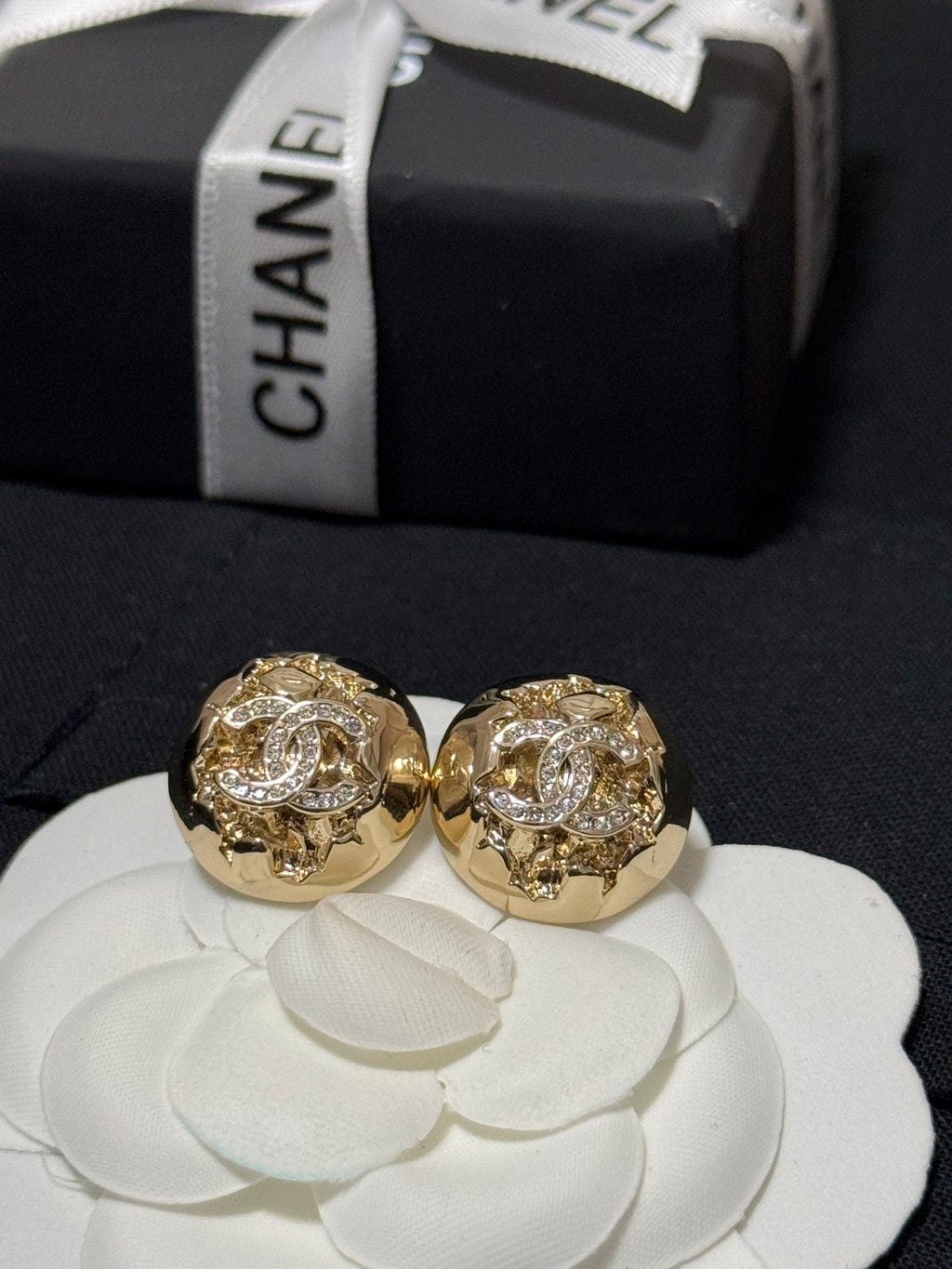 Gold-tone round stud earrings with crystal halo motif displayed on a white flower cushion