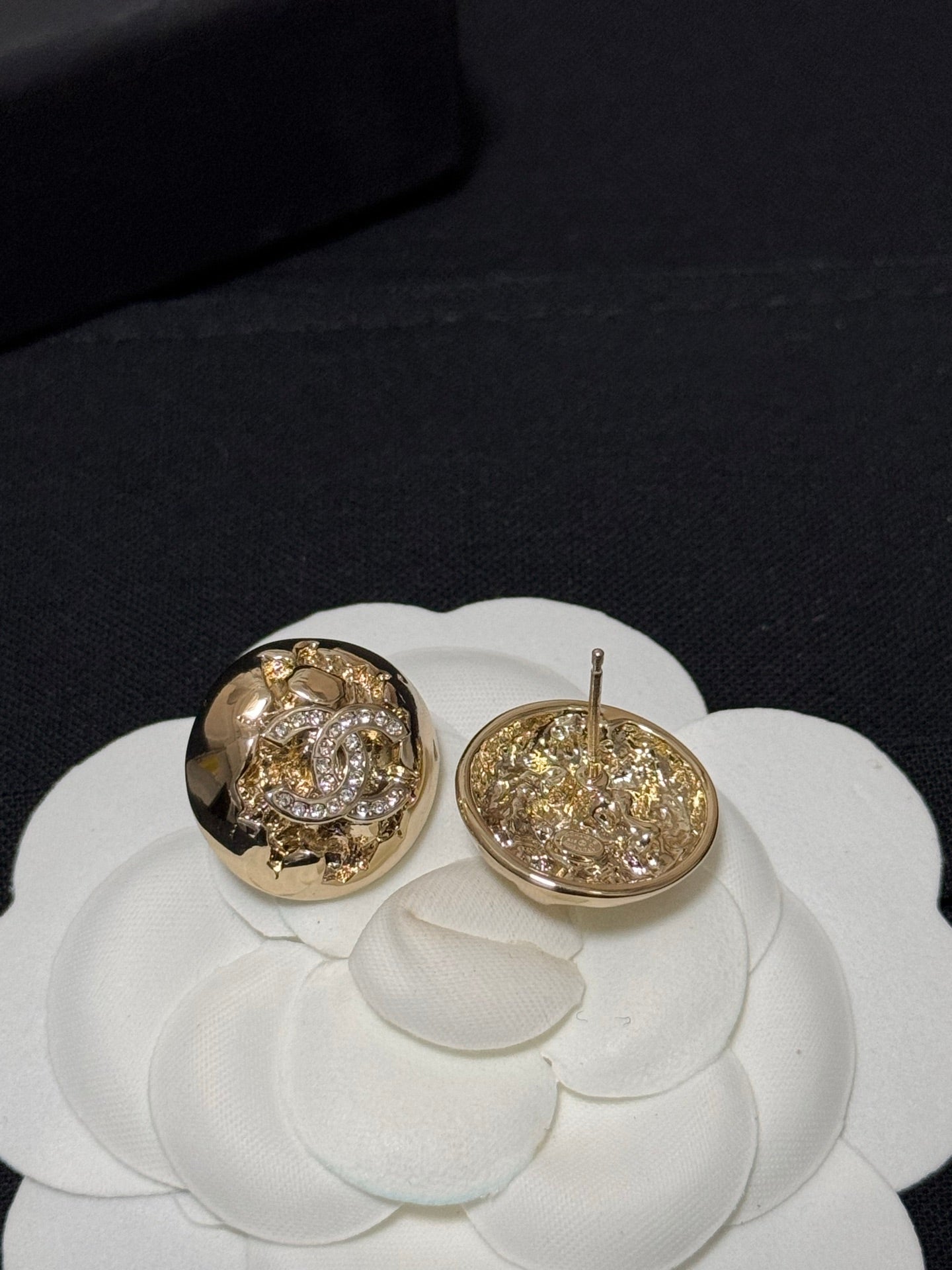 Gold-tone round stud earrings with crystal halo motif, one showing the post