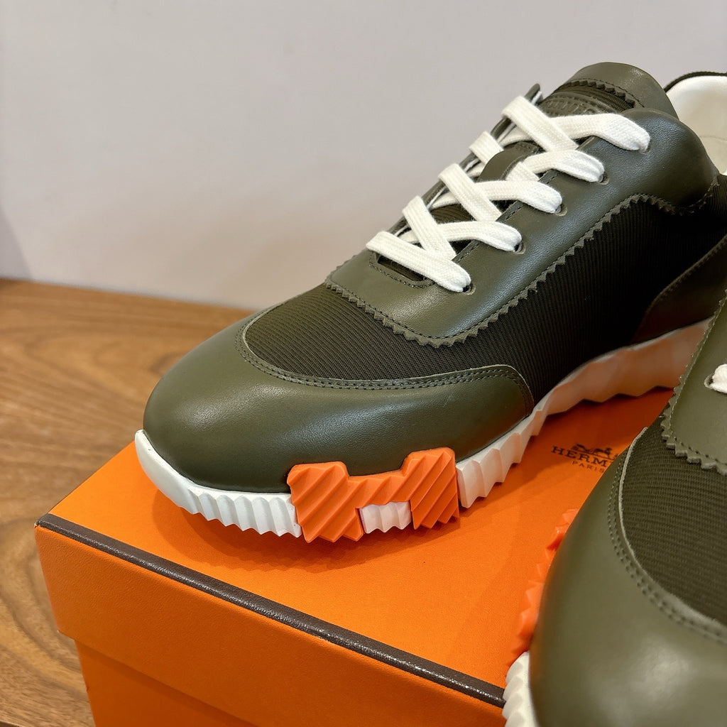 Olive green sneaker close-up with white laces and thick ridged white-and-orange sole