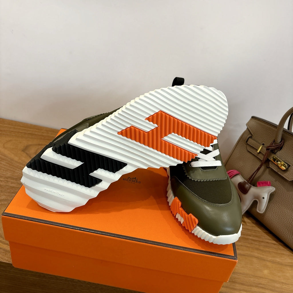 Sneaker outsole view: chunky white tread on olive green heel with orange accent