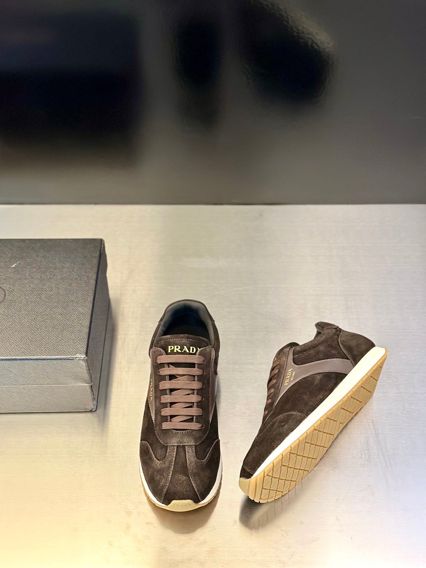 Prada unisex sneakers side view pair, dark brown suede with off-white rubber sole.