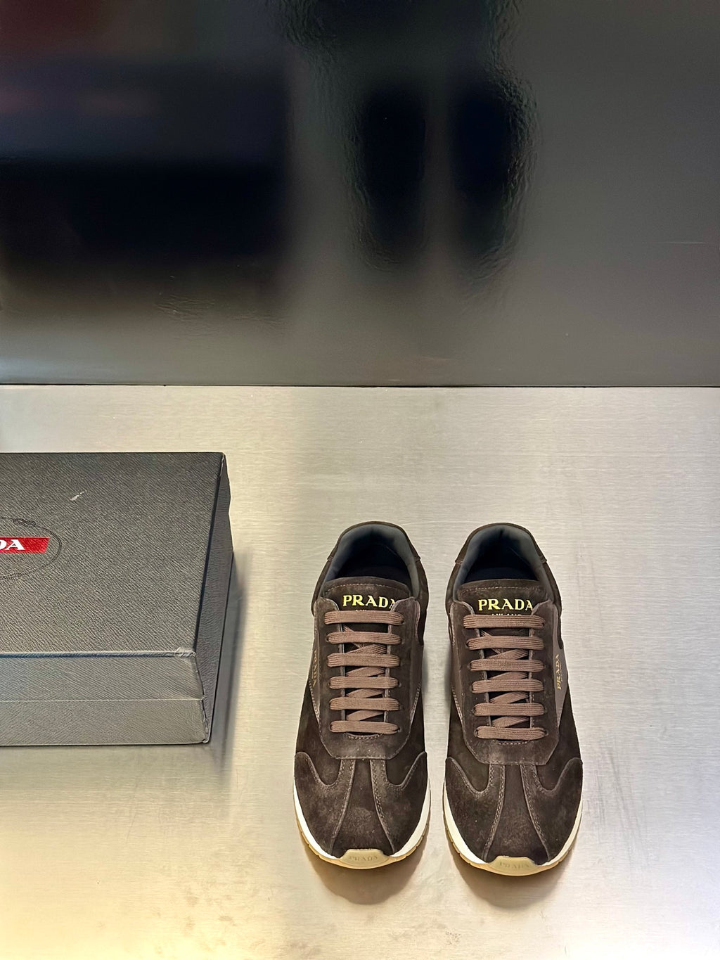 Prada unisex sneakers in dark brown suede with white sole and lace-up front.