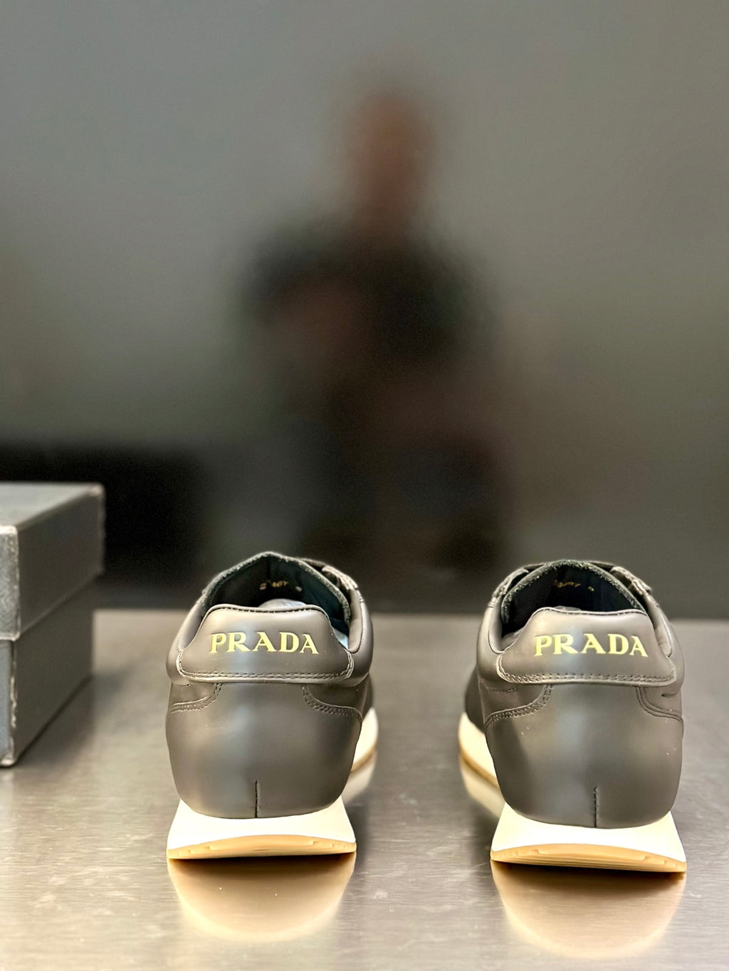 Prada leather sneaker pair in light gray, rear view with Prada logo on heel