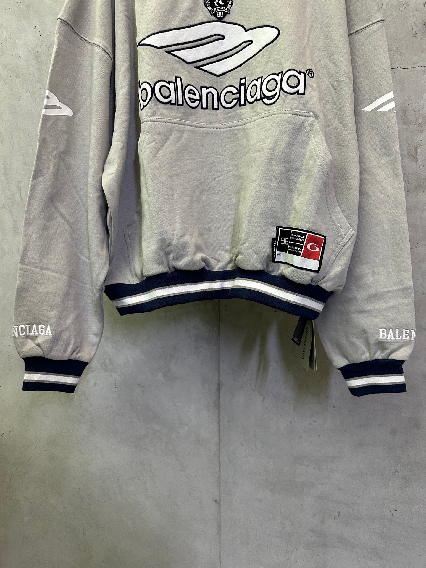 Light gray hoodie with large front Balenciaga graphic, patch detail, and striped cuffs