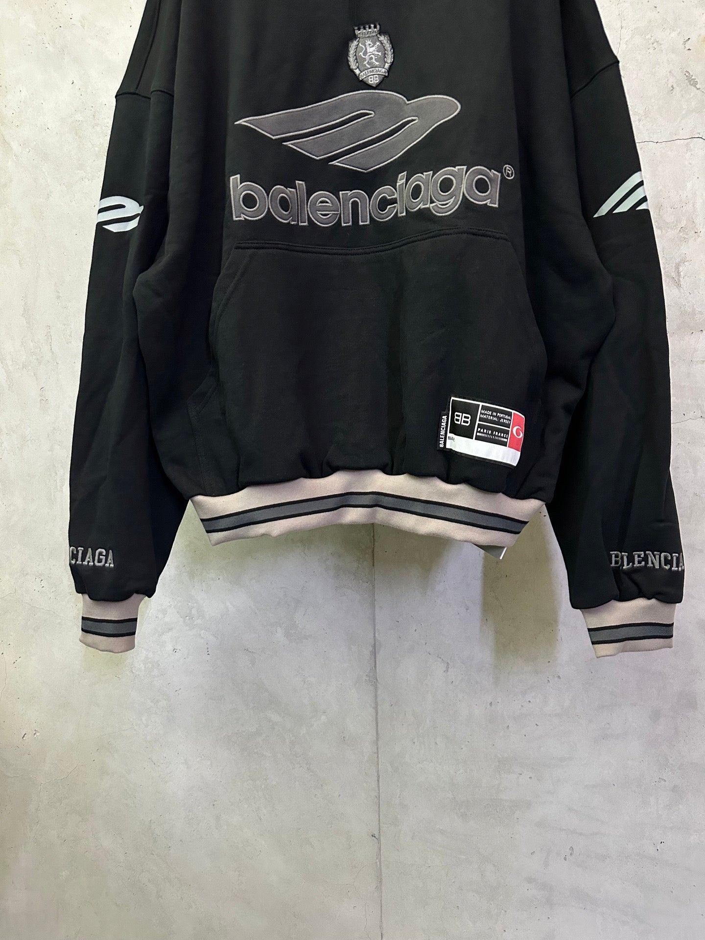 Black Balenciaga hoodie with front logo, crest, and striped cuffs and hem