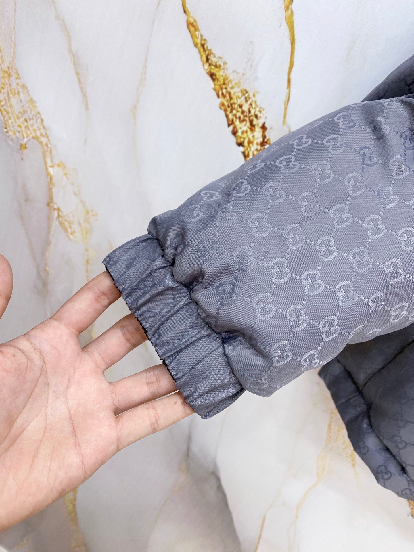 Gucci long puffer jacket cuff and sleeve seam, dark gray GG patterned fabric.