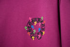 Purple T-shirt with small circular multicolor cross graphic on chest