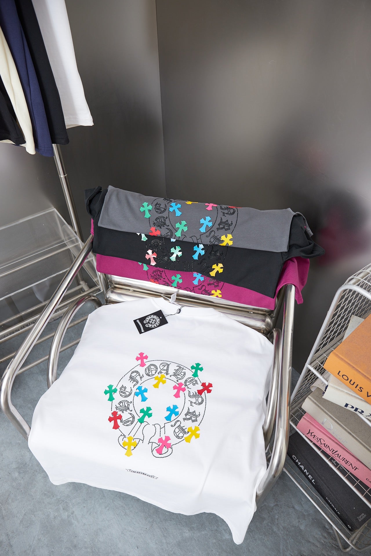 Folded graphic T-shirts on rack: white, dark gray and magenta with crosses