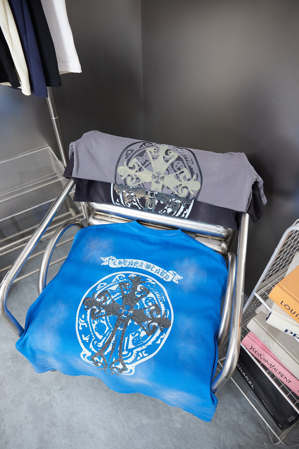 Folded T-shirts: one blue and one gray, each with large oval crest graphic