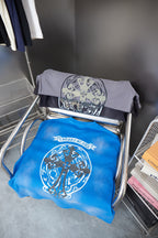 Folded T-shirts: one blue and one gray, each with large oval crest graphic