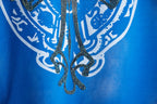 Blue T-shirt close-up of central crest with decorative swirls