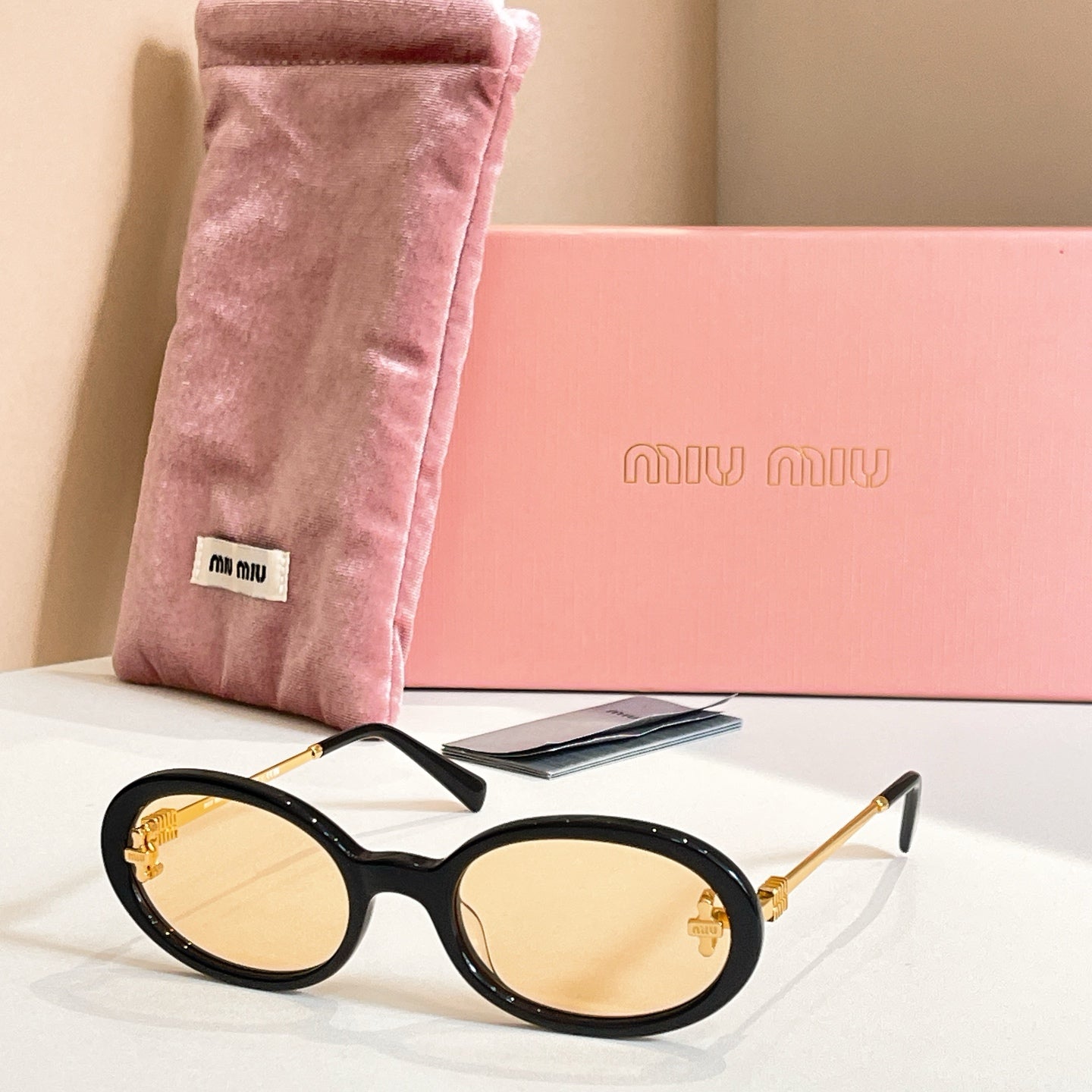 MiuMiu round sunglasses with black frames, gold accents, and light lenses