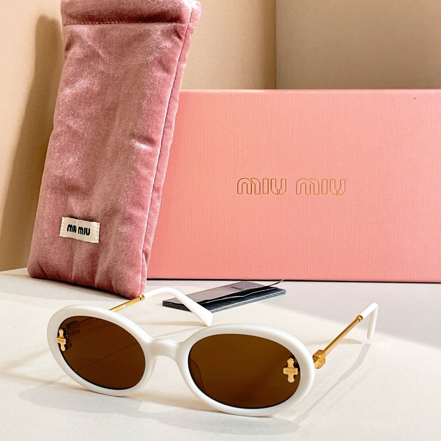 MiuMiu round sunglasses with white frames, gold accents, and brown lenses