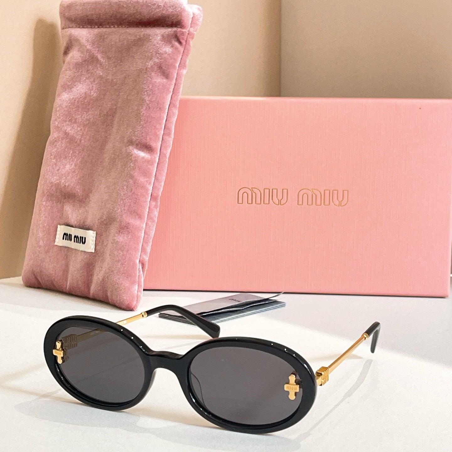 MiuMiu round sunglasses with black frames, gold accents, and dark lenses