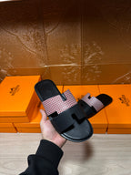 Hermes slide sandals on a hand: black sole with light patterned strap over the foot