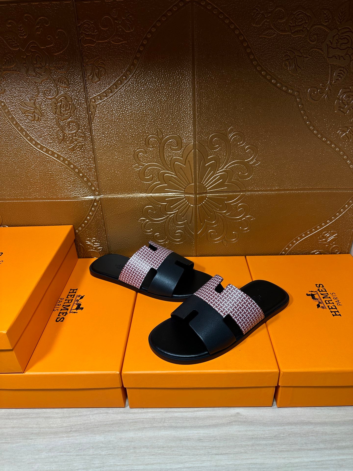 Hermes sandals with black slide sole and light patterned strap, placed on the box surface