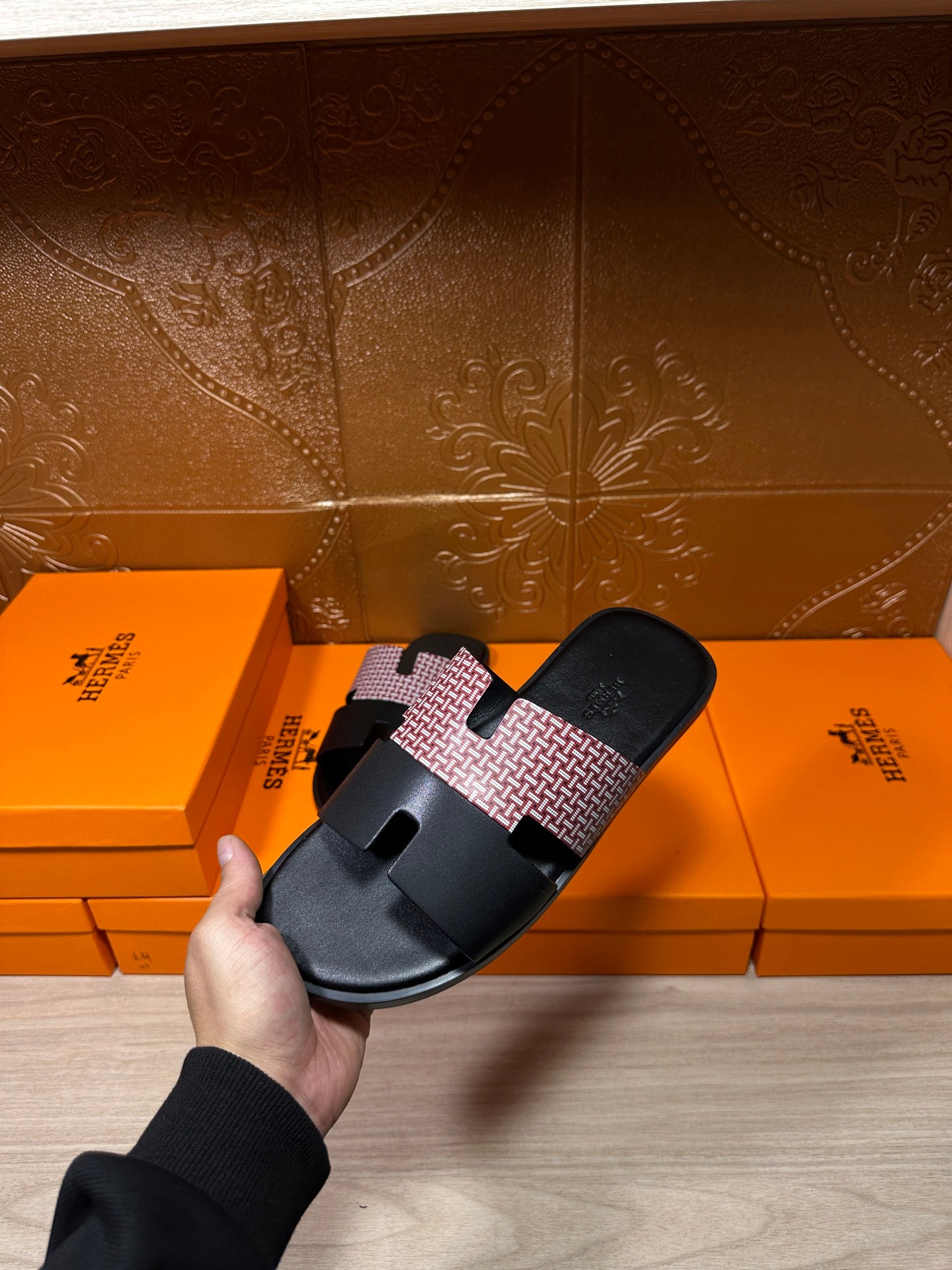 Hermes sandals held in hand, black slide sole with light patterned strap across top