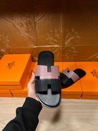 Hermes sandals held up: black footbed with light patterned cross strap and open toe