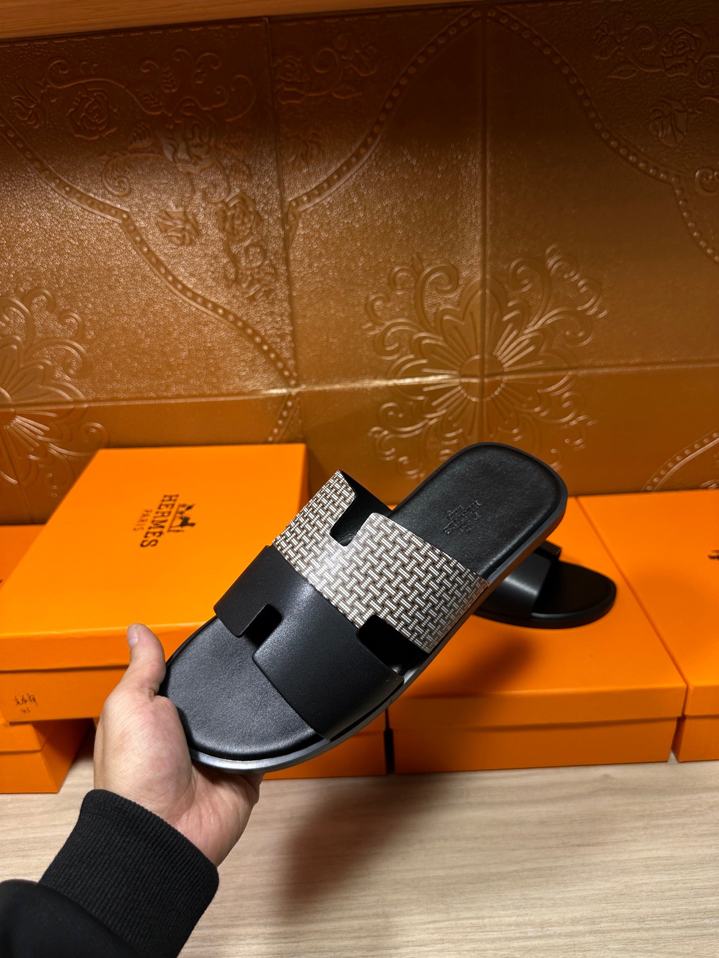 Hermes slide sandal held in hand: black base with woven gray strap and buckle tab