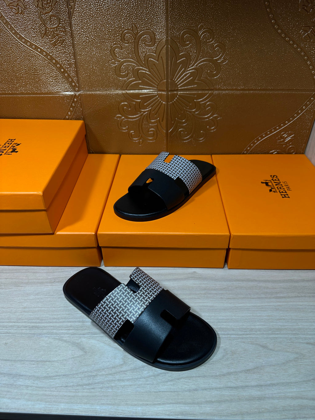Hermes slide sandals with black sole and gray textured strap, angled view on boxes