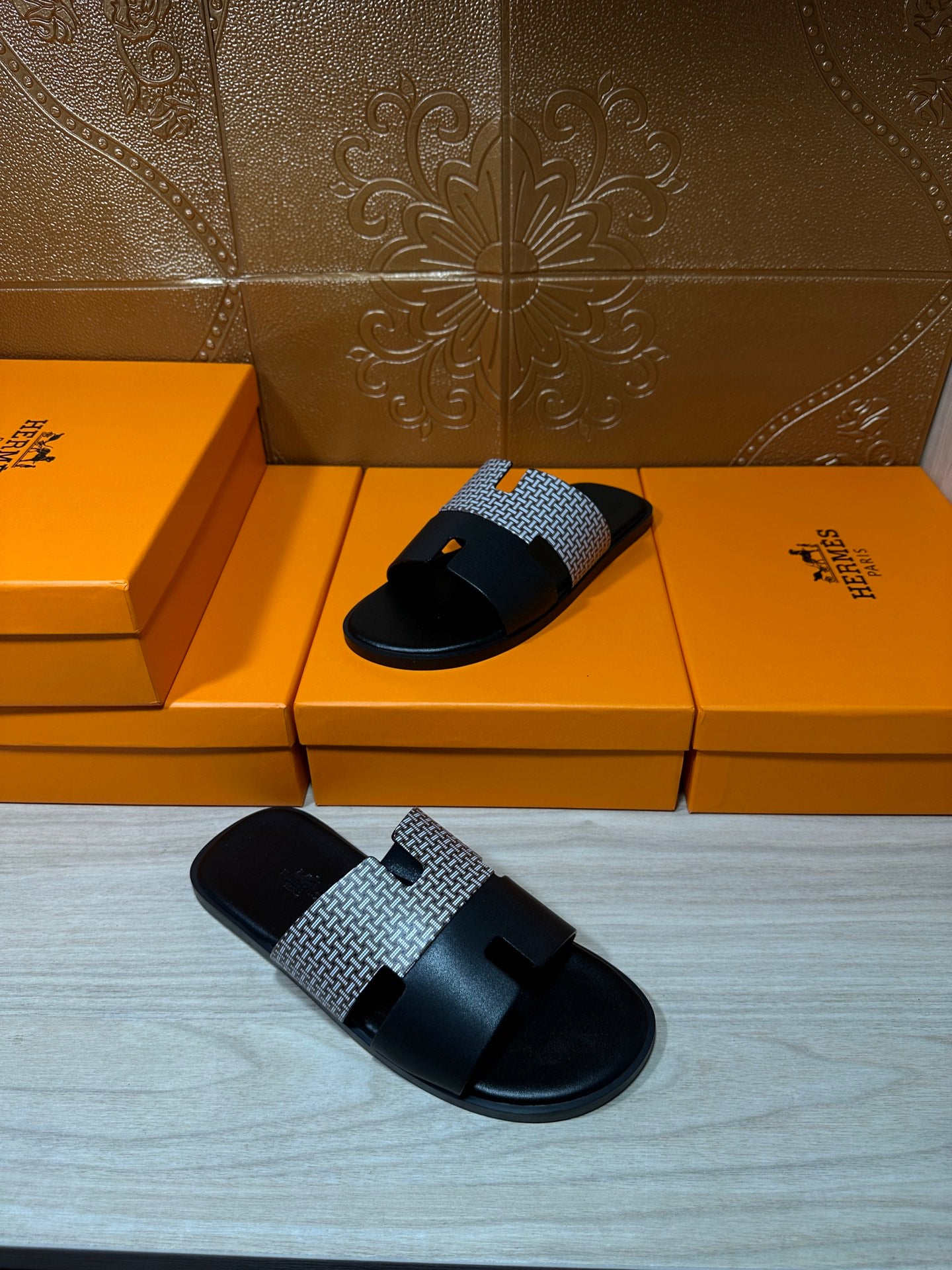 Hermes slide sandals with black sole and gray textured strap, angled view on boxes