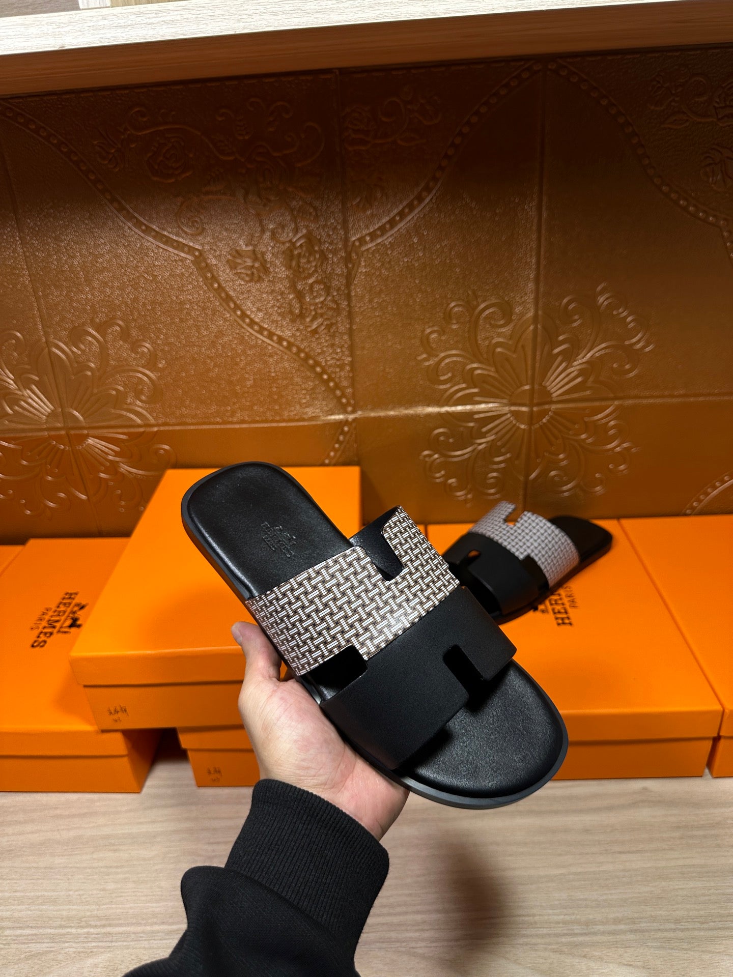 Hermes slide sandal held up: black footbed with patterned gray strap and wide buckle detail