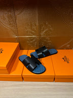 Hermes sandals with black straps and blue patterned footbeds, placed on orange storage boxes.