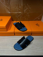 Hermes sandals with black leather straps and blue patterned footbeds, arranged on orange boxes.
