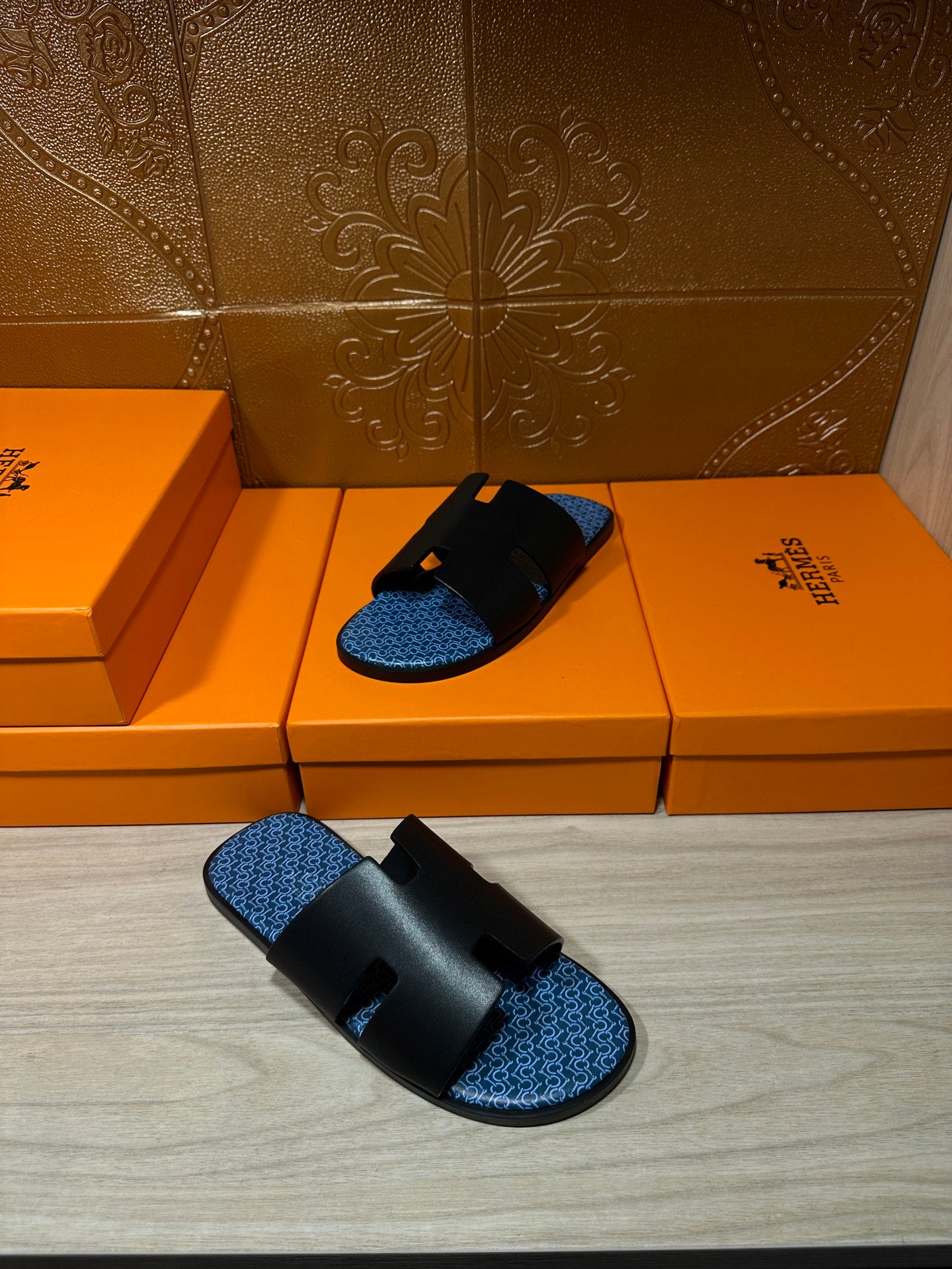 Hermes sandals, one pair and one shoe on orange boxes; black straps with blue footbeds.