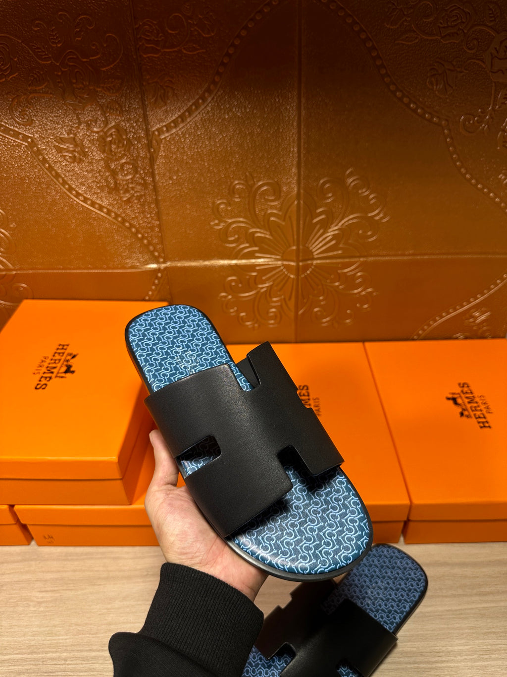 Hermes sandals held in a hand: black straps over blue patterned footbed, with sock cuff.