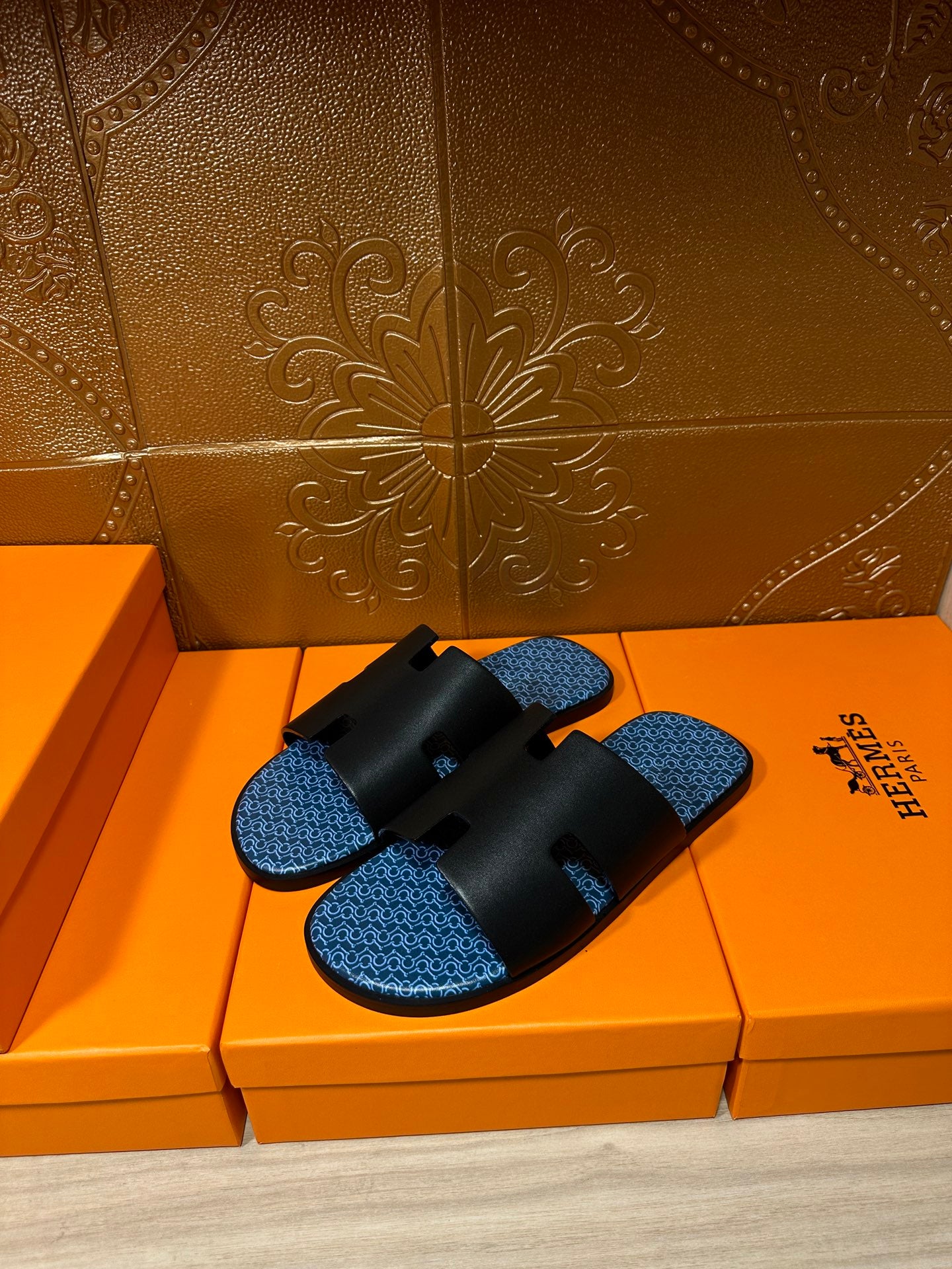 Hermes sandals with black double straps and blue textured footbeds, laid on orange boxes.