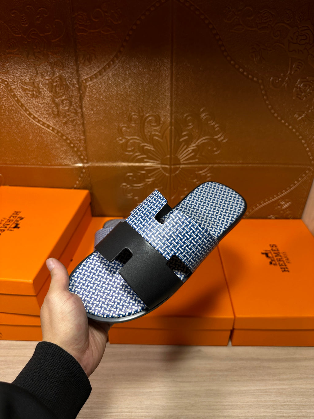 Blue woven slide sandal with black strap band and buckle, held and angled