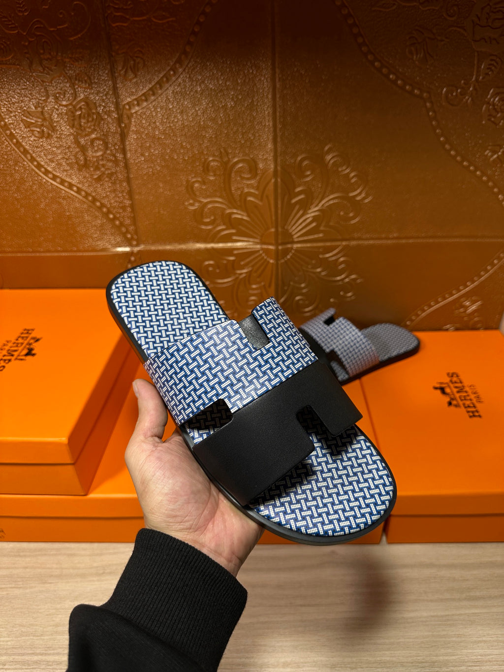 Blue woven slide sandal with black cross strap and buckle, held in hand