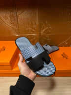 Blue woven slide sandal with black cross strap and buckle, held in hand