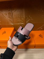 Pink textured slide sandals with black buckle strap; side view held in hand