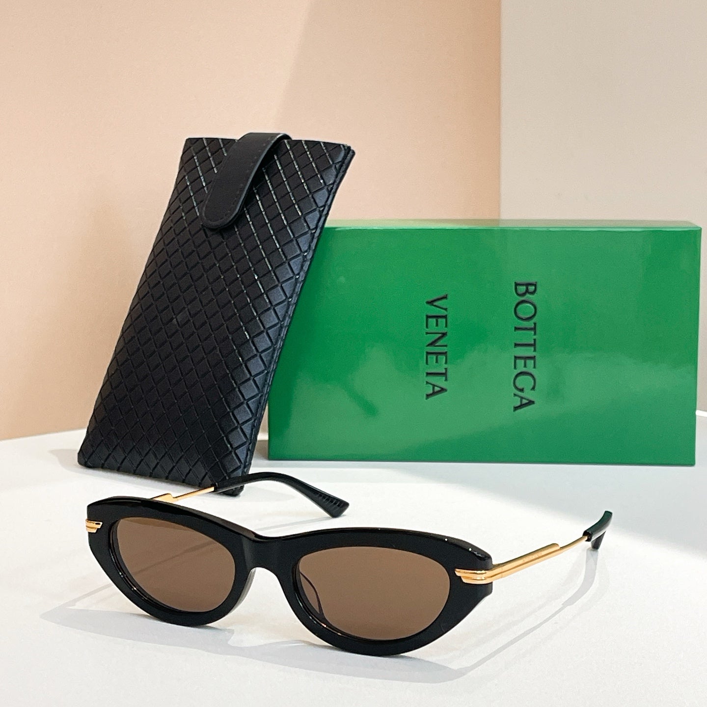 Black cat-eye sunglasses with gold-tone temples and dark lenses, with black textured case